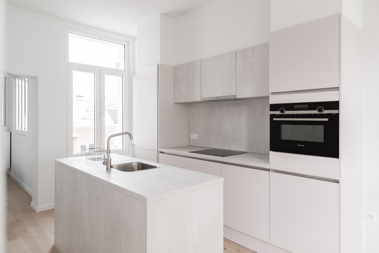 Lichte keuken met betonlook bovenkasten en een eiland met spoelbak, voor een hoog raam