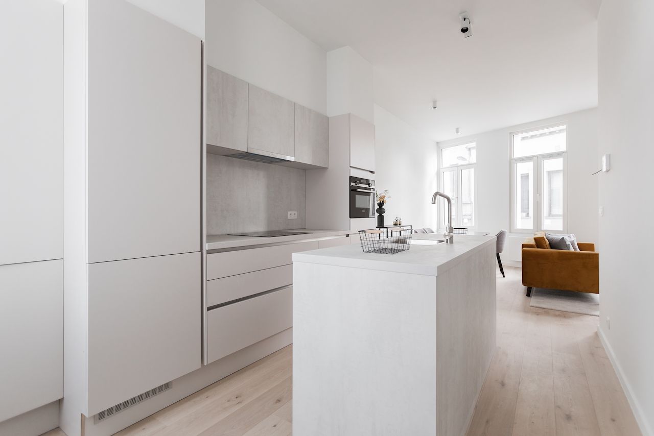 Lichte keuken met een eiland in betonlook en een doorkijk naar de leefruimte