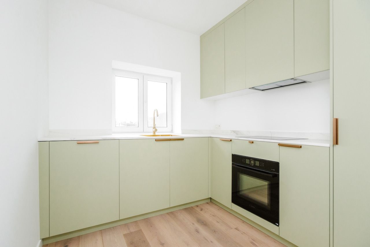 Saliegroene L-keuken met koperen grepen en een spoelbak onder het raam