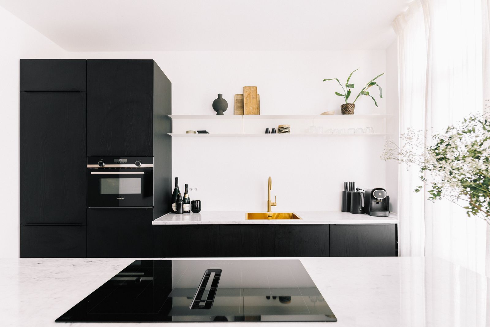 Zwarte keuken met een marmeren eiland, messing kraan en open legplanken, een realisatie van Cervano in Antwerpen